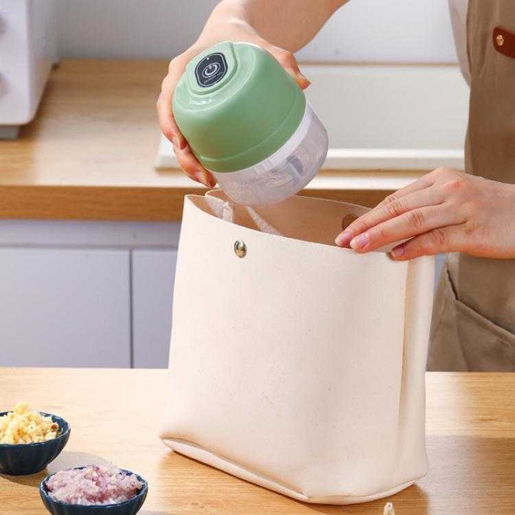 Green rechargeable mini food chopper in hand being set into a tote bag
