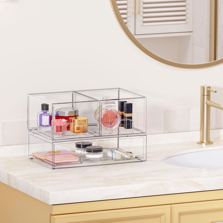 Transparent stackable cosmetic organizer with open compartments on countertop near mirror
