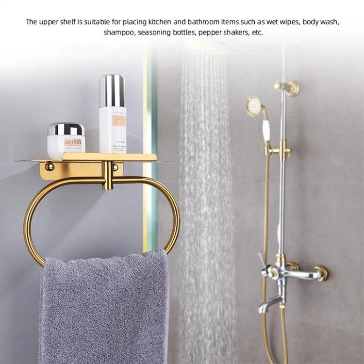 Gold stainless steel towel ring with shelf for holding bathroom towels.