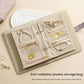 Beige jewelry organizer book open with clear compartments and slots for necklaces and rings.