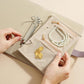 Beige jewelry organizer book open with snap rings and zipper compartments holding pearl jewelry.