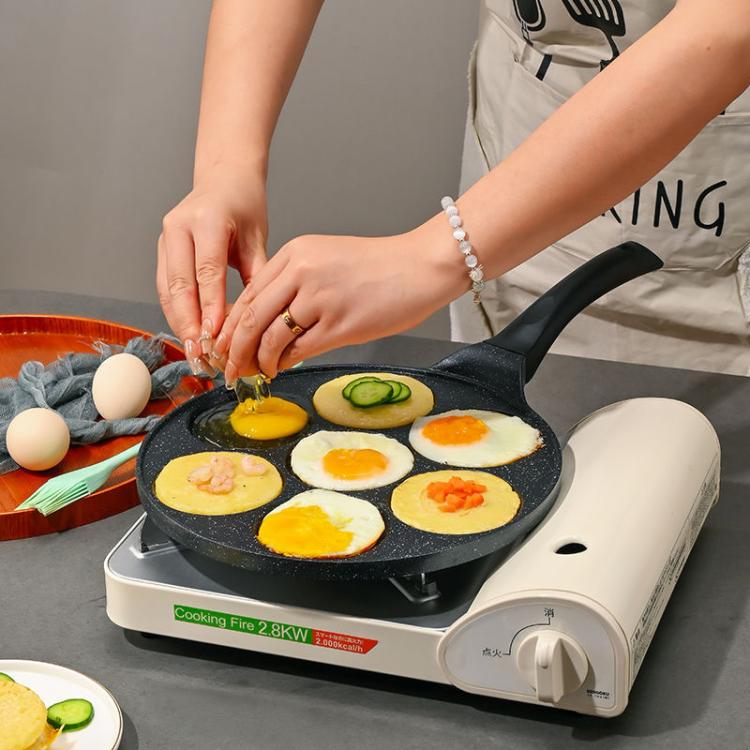 Nonstick 7-cup egg burger pan with fried eggs in wells on a small tabletop griddle.