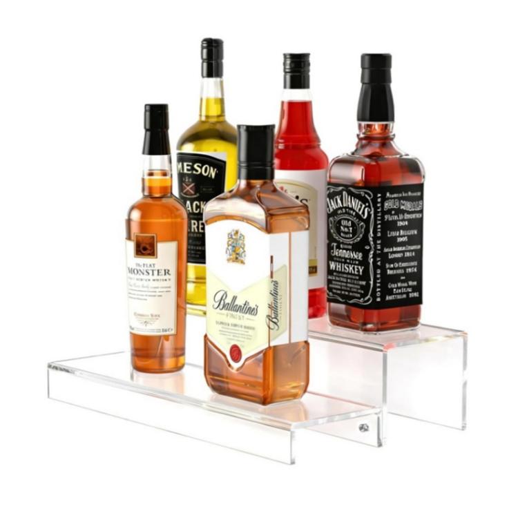 Clear acrylic 2-tier bottle rack holding liquor bottles on both shelves