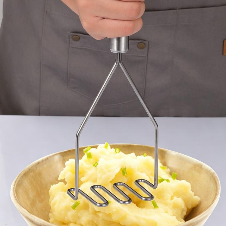 Stainless steel potato masher with wavy tines, held over a bowl of mashed potatoes.