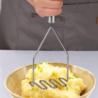 Stainless steel potato masher with wavy tines, held over a bowl of mashed potatoes.