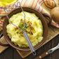 Stainless steel potato masher with wavy tines mashing potatoes in a serving bowl.
