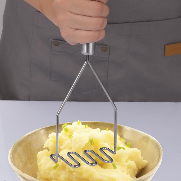 Stainless steel potato masher with wavy tines above a bowl of mashed potatoes.