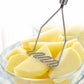 Stainless steel potato masher tines pressing potato pieces in a glass bowl.