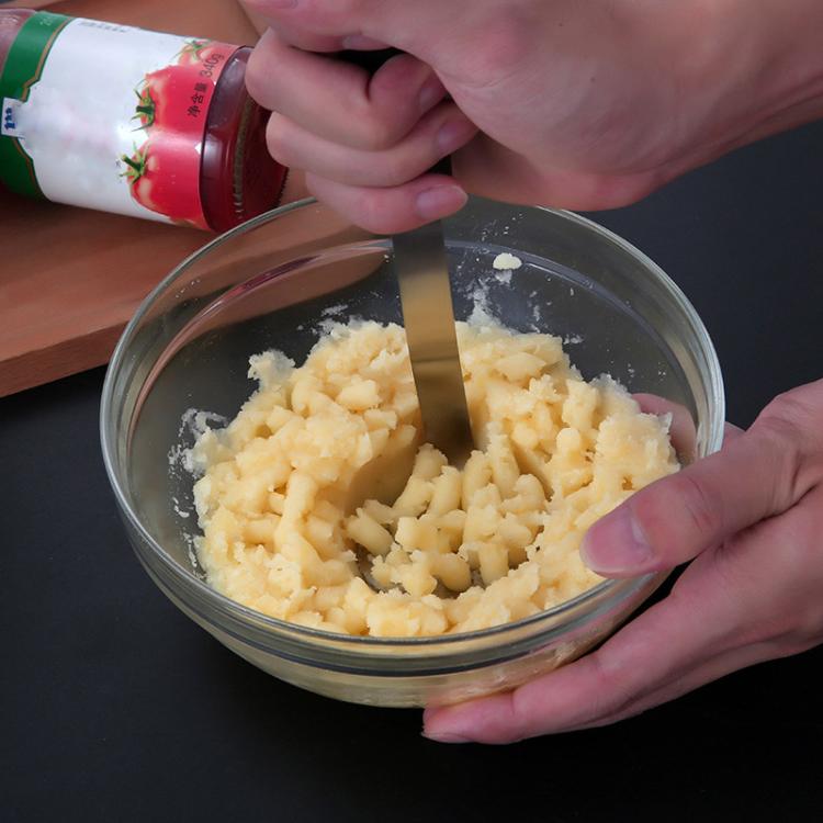 Potato masher in use: stainless disc and black handle crushing potatoes in bowl.