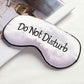 White satin sleep mask with “Do Not Disturb” lettering and black border
