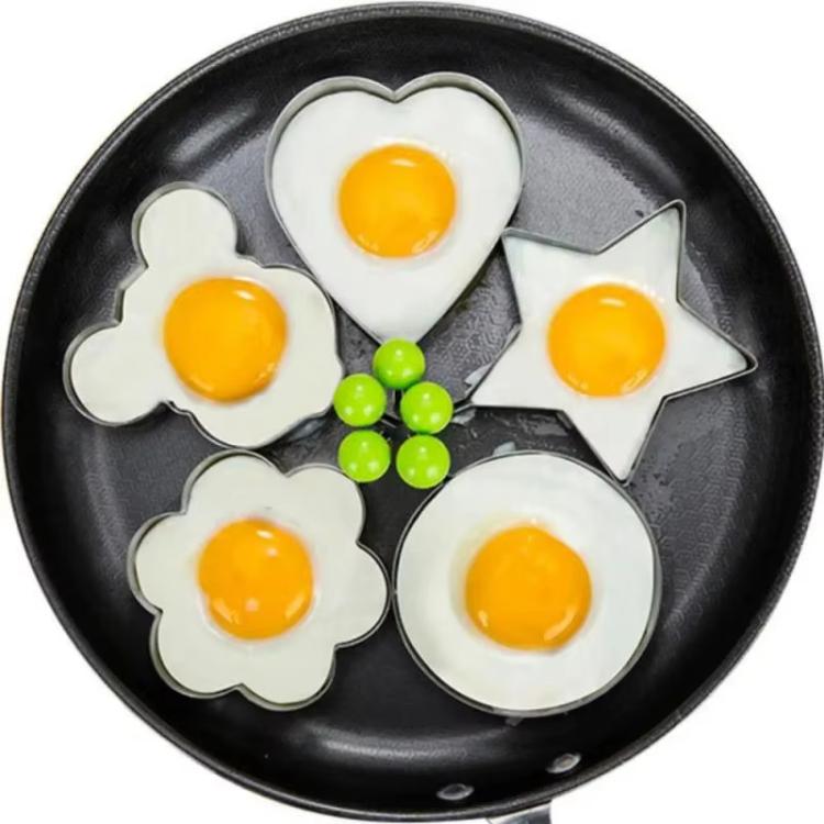 Sunny-side eggs shaped in flower, heart, star, and clover molds on skillet