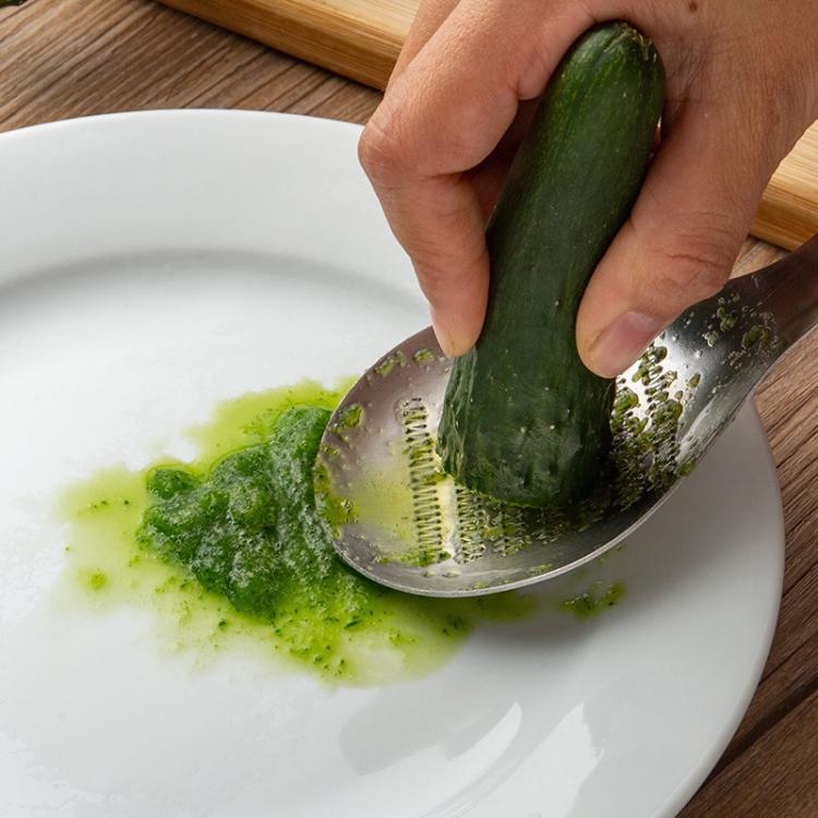 Perforated stainless steel grinder spoon grating a green vegetable onto a plate