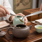 Stainless steel tea tongs lifting tea leaves above a green kettle