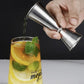Stainless steel jigger pour cup tilted over drink