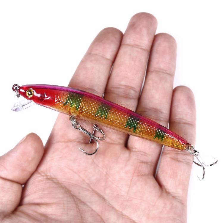 Small minnow fishing lure in hand: red-orange body with green pattern and treble hooks