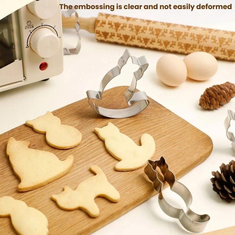 Stainless steel cat cookie cutters with several cut dough shapes on a wooden board