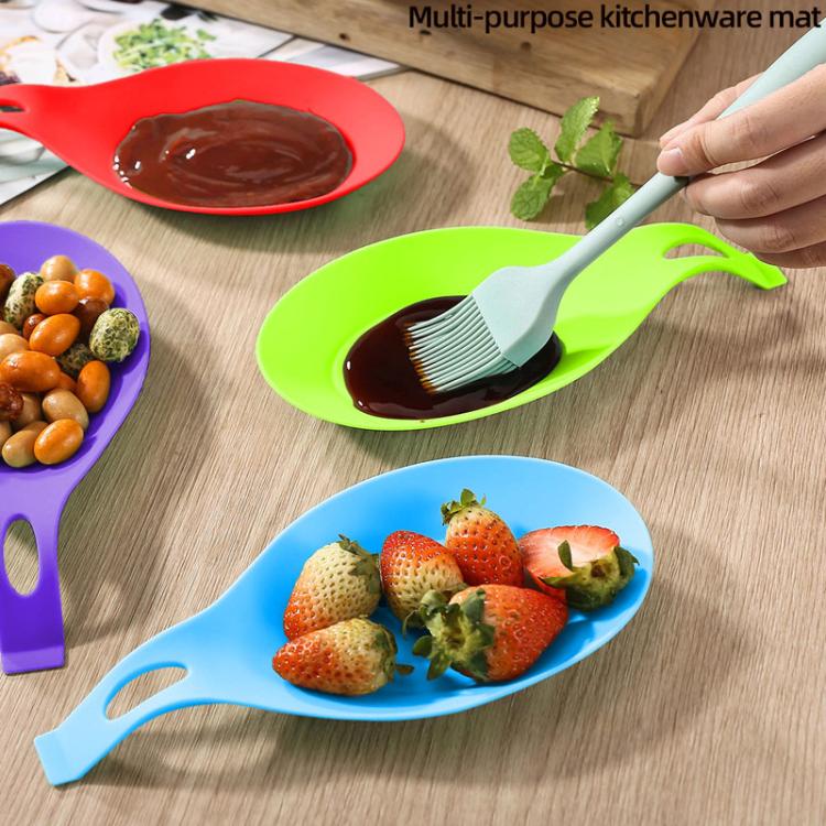 Green kitchen mat holding a utensil, with a raised rim and rounded leaf shape