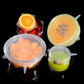 Clear silicone food storage lids covering bowls of fruit, round with tab handles