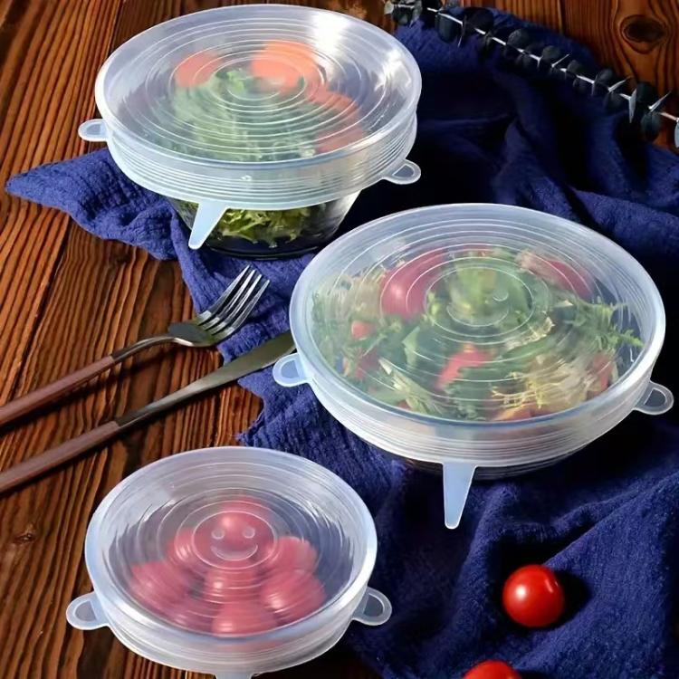 Clear round silicone food storage lids set, covering salads and vegetables on a table