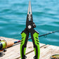 Green fishing line cutting shears with hook remover, shown outdoors on a dock.