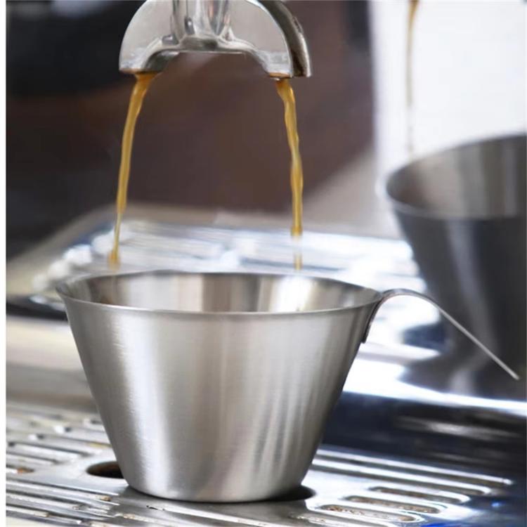 Stainless steel coffee cup with pointed spout pouring into another cup on drip tray