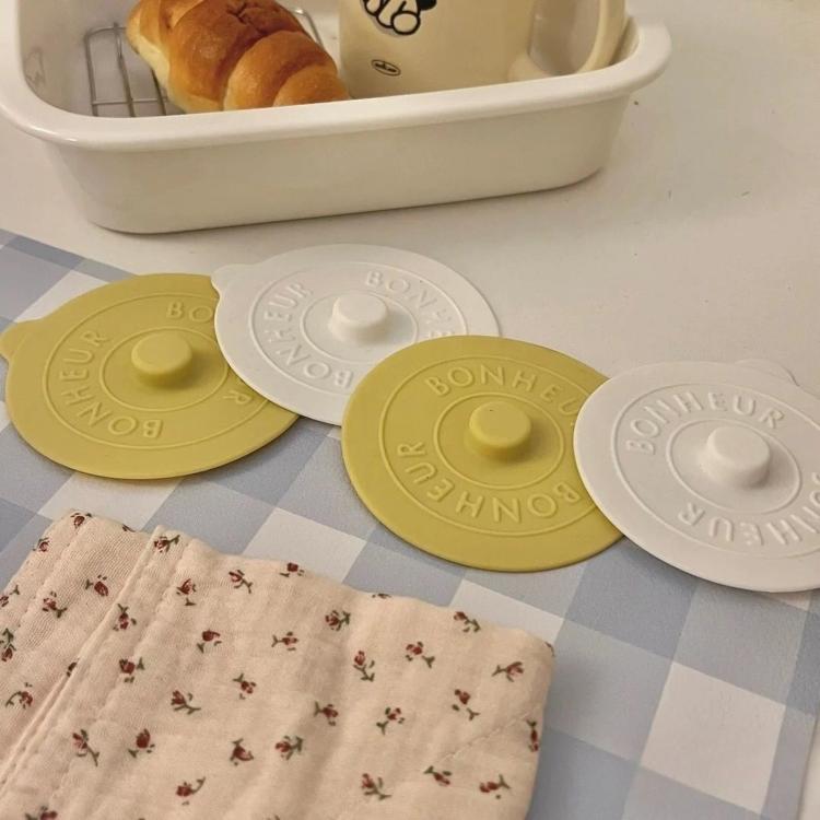 Round silicone lids in yellow, gray, and white with central knob, stackable fit