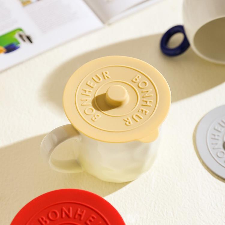 Yellow round silicone lid with central knob and embossed BONHEUR text