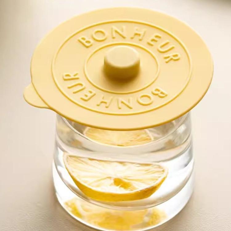 Yellow round silicone lid with raised center knob and embossed BONHEUR text