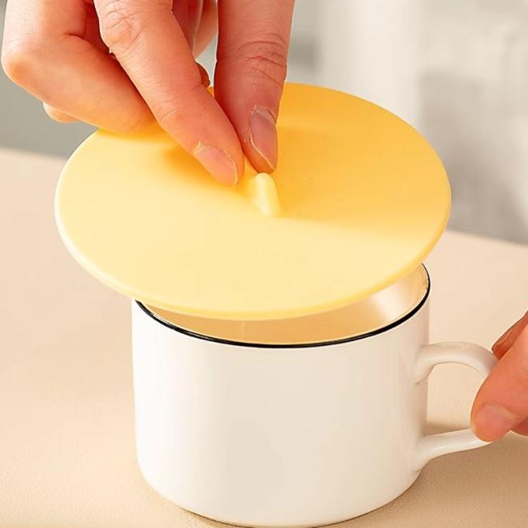 Yellow round silicone cup lid being pressed onto a white mug with handle