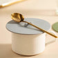Light gray silicone cup lid with center tab on a white cup with gold spoon