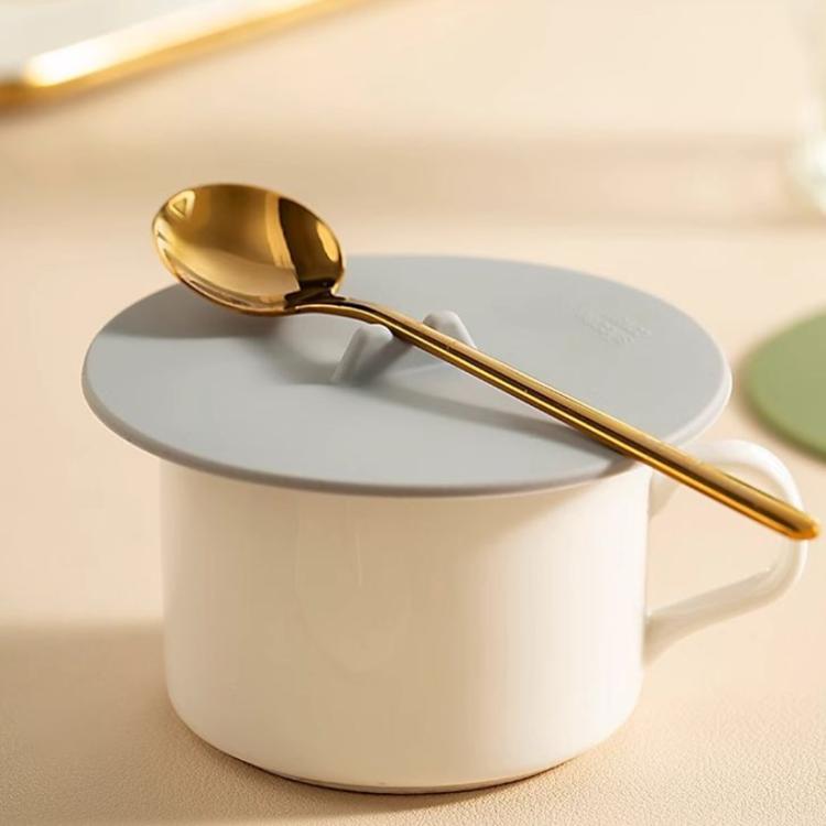 Light gray silicone cup lid with center tab on a white cup with gold spoon