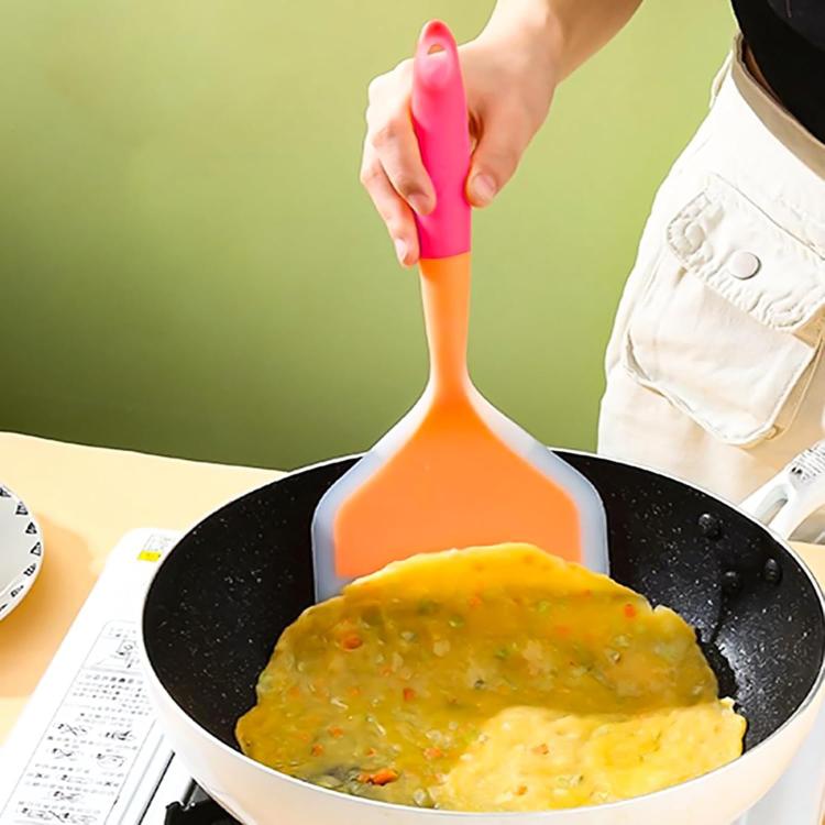 Wide-mouth silicone tamagoyaki spatula with orange and pink handle, used in a skillet