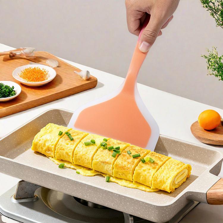 Orange silicone egg spatula with pink handle, spreading rolled omelet on a pan