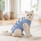 Blue cat recovery suit with bow-trimmed straps on kneeling pet