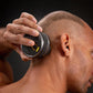 Electric shaver head held to a bald scalp, five foil cutters visible