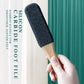 Foot callus remover held in hand, featuring dark abrasive pad on bamboo handle