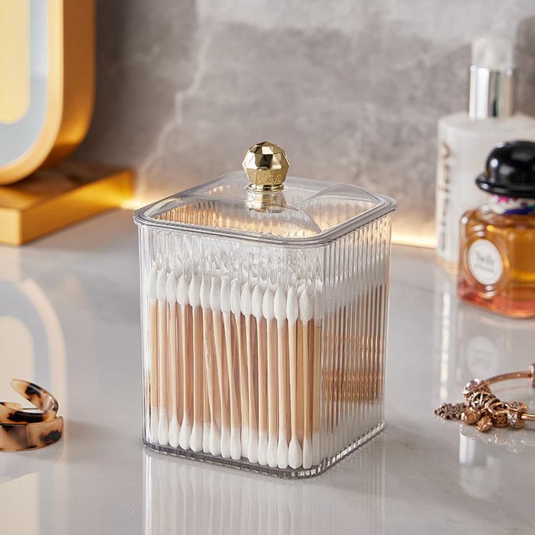 Clear plastic cotton swab holder with square lid and gold knob, filled with cotton swabs