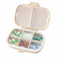 Wheat-straw pill organizer case open with clear dividers holding green, blue, and red pills
