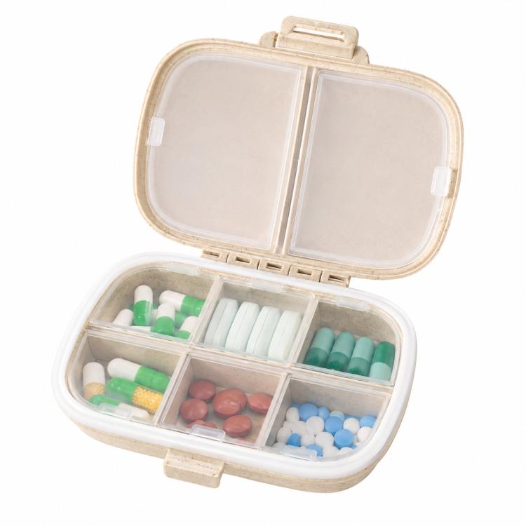 Wheat-straw pill organizer case open with clear dividers holding green, blue, and red pills