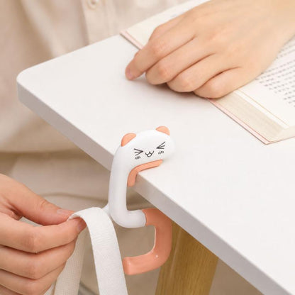 Cat-shaped foldable table bag hook on a desk edge, white with peach handle.