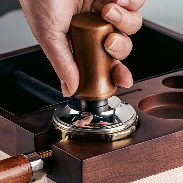 Wood-handled constant force coffee tamper pressing into portafilter base