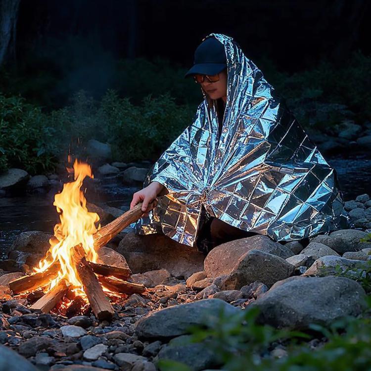 Silver emergency thermal blanket wrapped outdoors beside a campfire