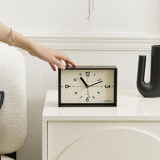 Woodgrain desktop clock with cream face, black numerals, and black hands on a shelf.