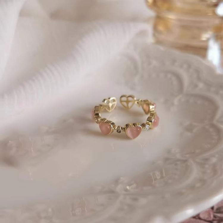 Close-up of adjustable gold-tone heart ring with pink cat-eye stones and sparkle hearts