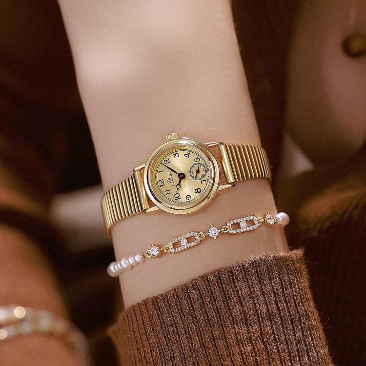 Gold-tone small round watch on wrist with ribbed expansion band and seconds subdial