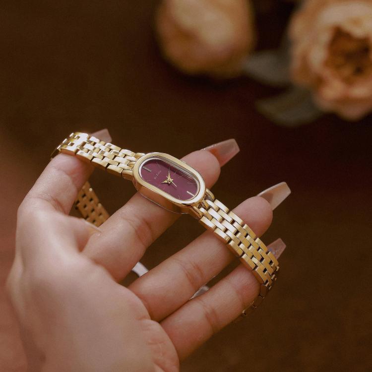 Silver metal oval quartz dress watch with maroon dial on a wrist