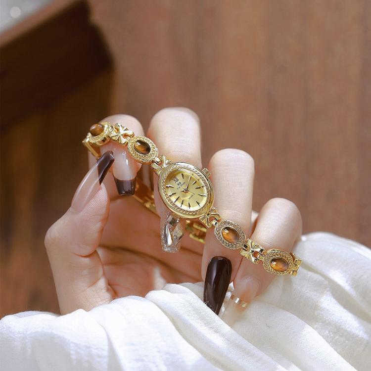 Gold oval analog quartz bracelet watch held on fingers with brown stone accents