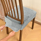 Gray velvet stretch chair seat cover with buckle straps, being fitted on dining chair
