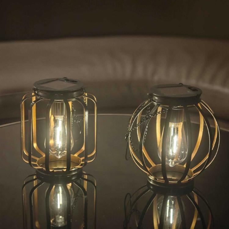 Two hanging black lanterns with warm bulbs on a wall shelf
