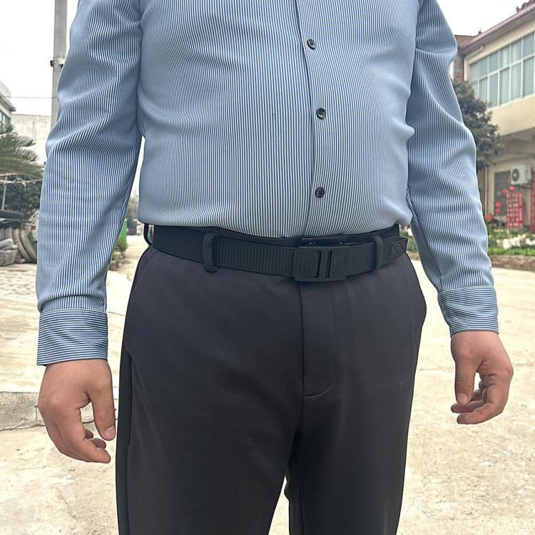 Black nylon web belt with automatic buckle worn at the waist with dark trousers
